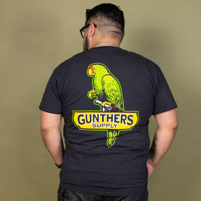 Person wearing a black t-shirt with a green parrot graphic and 'Gunthers Supply' text on the back.