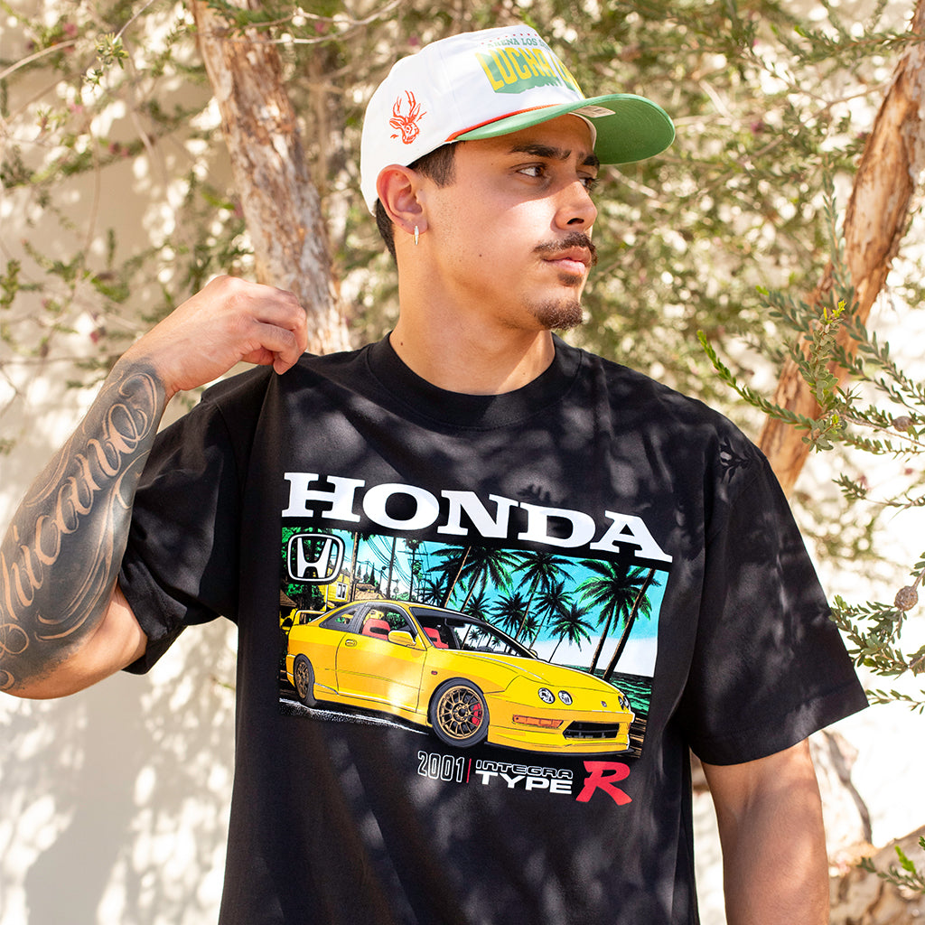 Person wearing a black Honda t-shirt with a yellow car graphic outdoors.