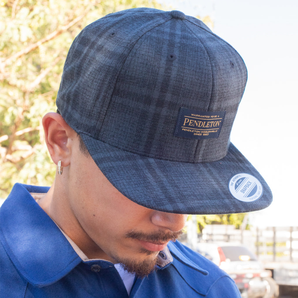 Person wearing a blue plaid Pendleton cap with a blurred outdoor background
