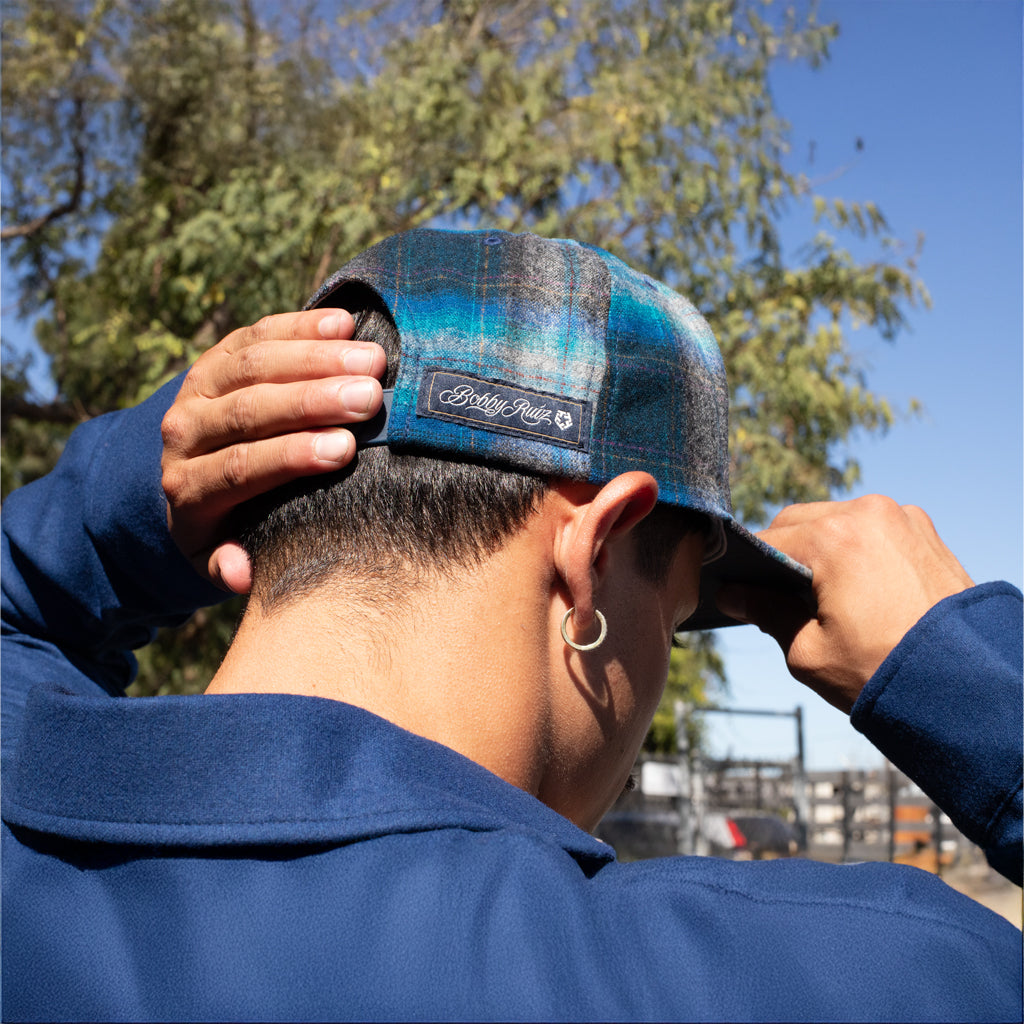 Person wearing a blue plaid cap with a brand logo, outdoors on a sunny day.