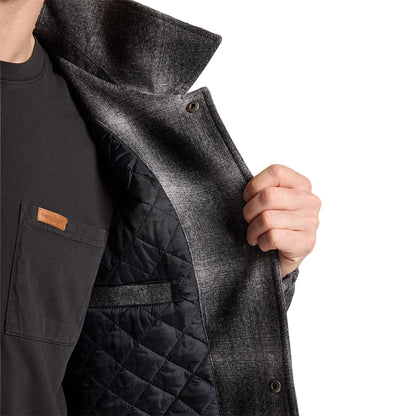 Person wearing a dark gray coat with a quilted black lining on a light gray background