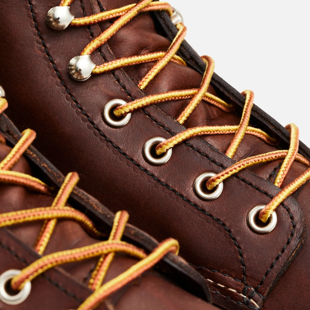 Close-up of brown leather boot with orange laces and metal eyelets on a white background