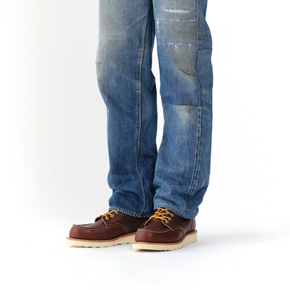 Brown leather shoes with white soles worn with blue jeans on a white background