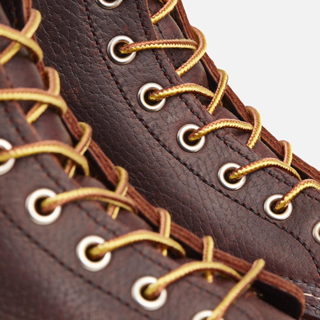 Close-up of brown leather boots with gold laces on a light gray background