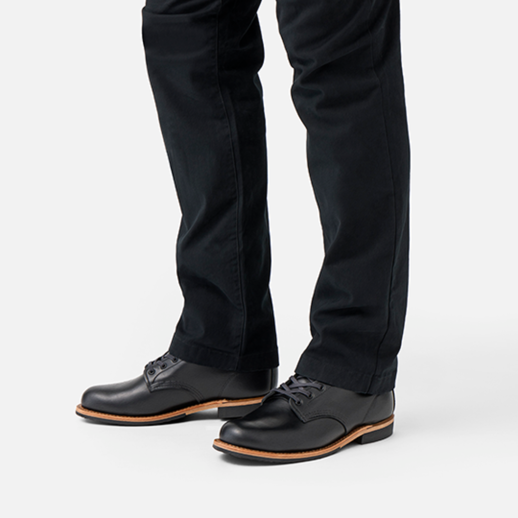 Black dress shoes with brown soles worn with black pants on a white background