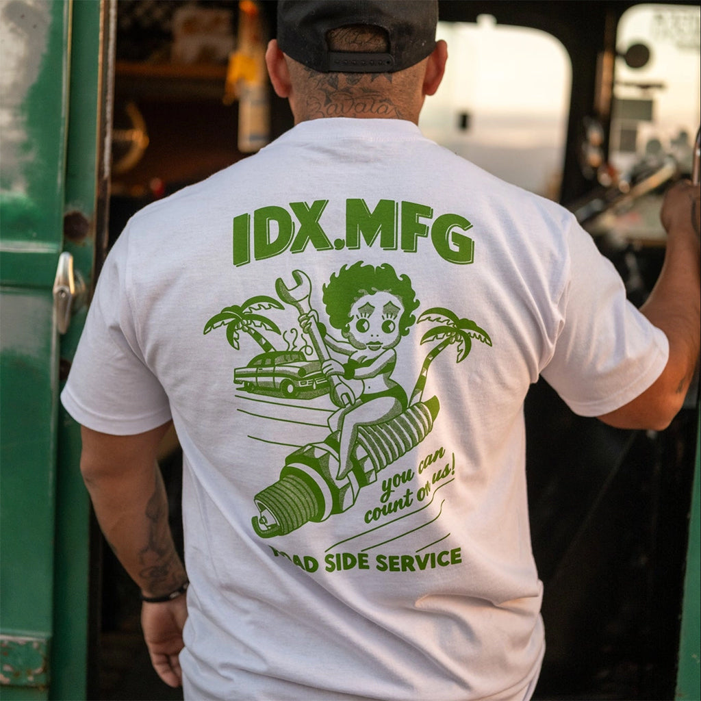 Person wearing a white t-shirt with green graphics and text, standing next to a green vehicle.