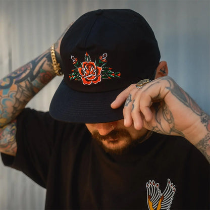 Person wearing a black cap with a floral design, adjusting it against a neutral background.