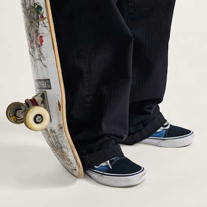 Person wearing black pants and blue sneakers standing next to a skateboard with a colorful design.