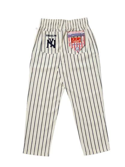 A pair of Cookman brand baseball-style pinstripe pants in cream with thin black stripes.