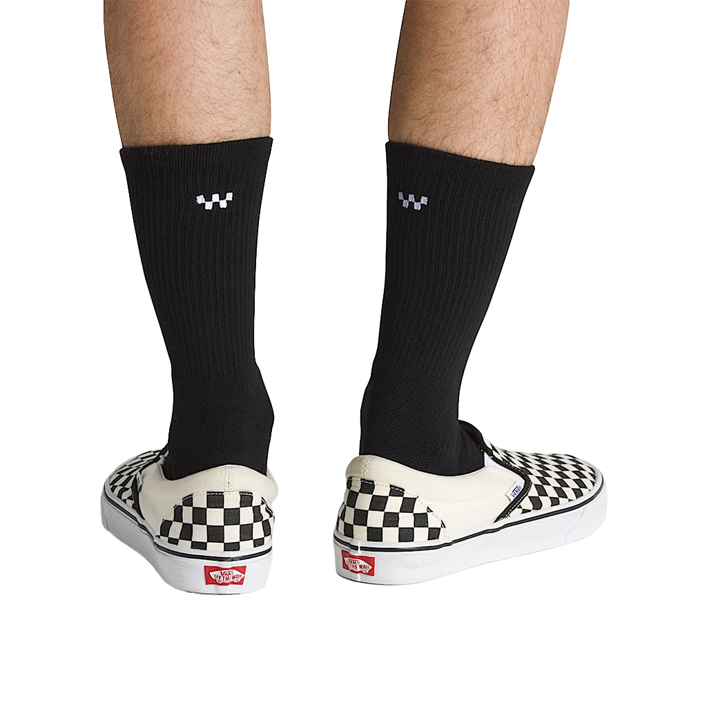 Black socks with a logo worn with checkered Vans shoes on a white background