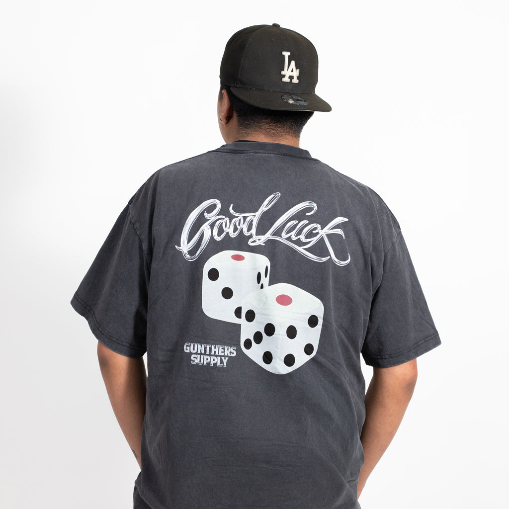 Person wearing a dark gray t-shirt with 'Good Luck' and dice design, standing against a white background.