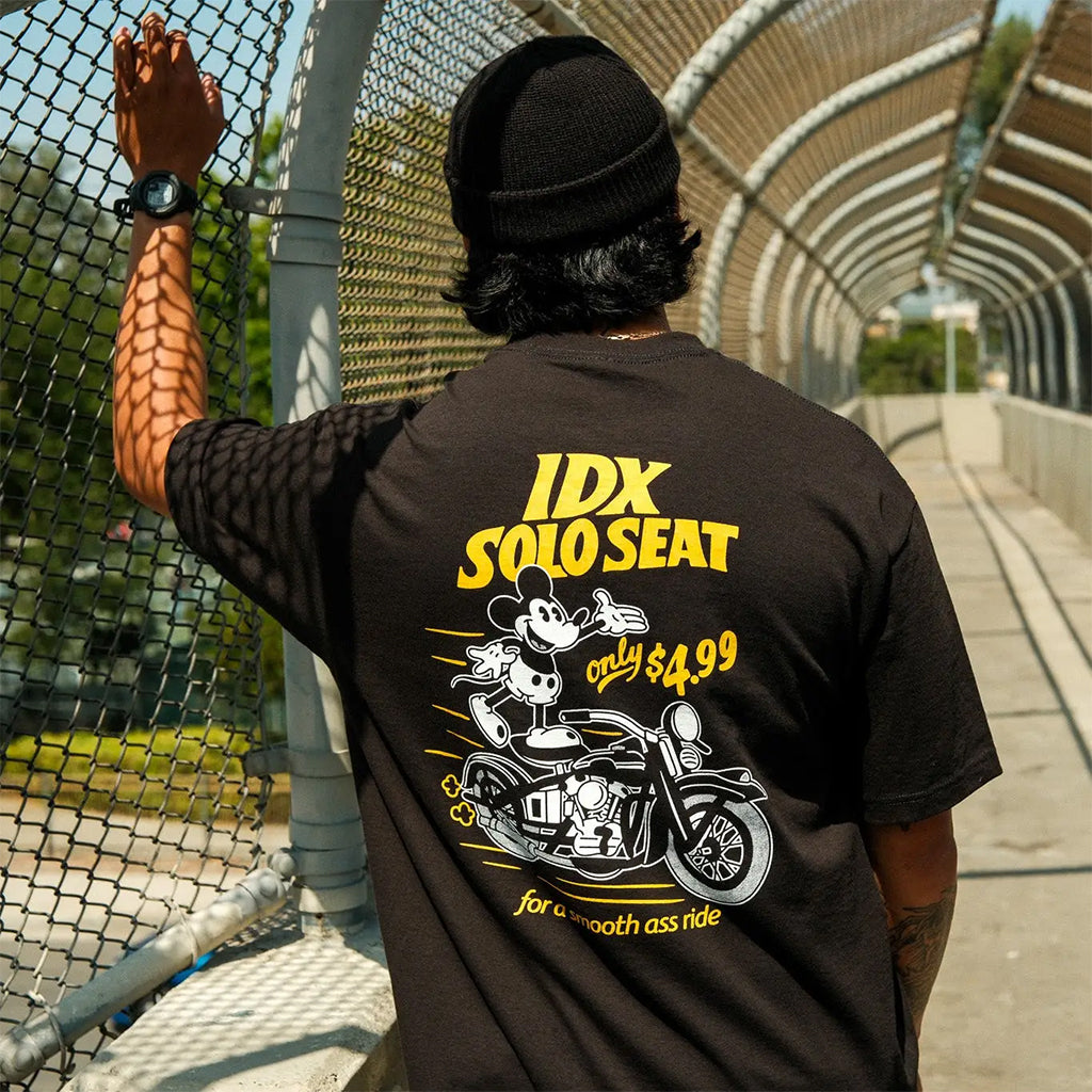 Person wearing a black t-shirt with yellow and white graphics and text, standing outdoors.
