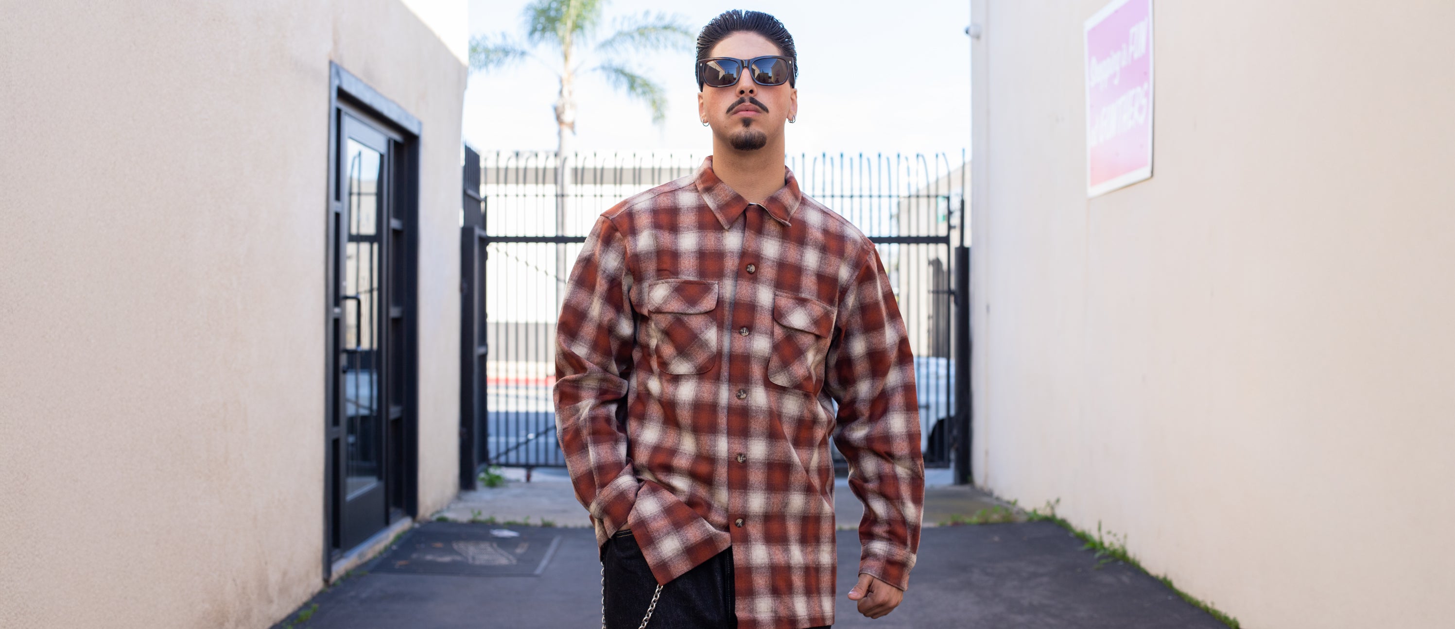 Man wearing a plaid shirt standing in an alleyway.