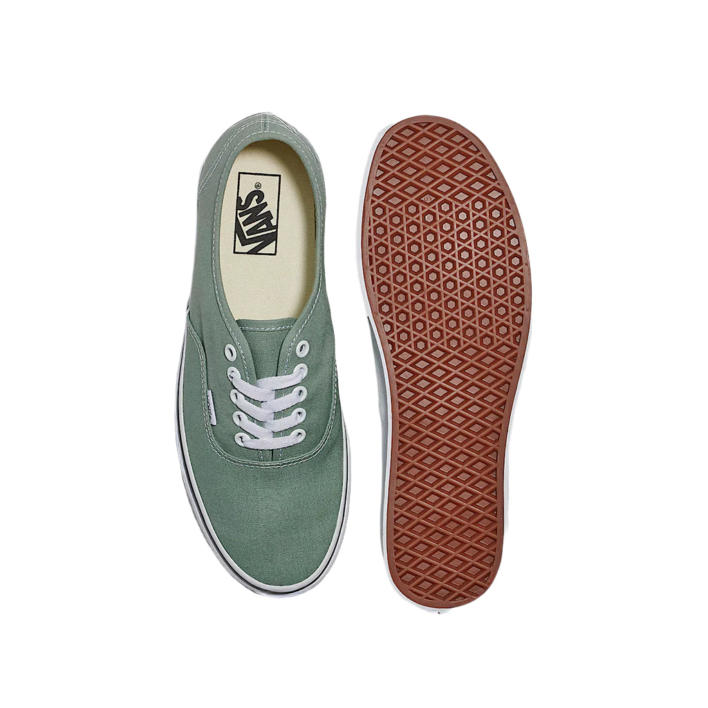 Green sneaker with white laces and brown sole on a light gray background