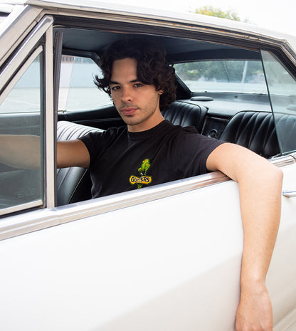 Man sitting in a classic car wearing a black t-shirt with a logo.