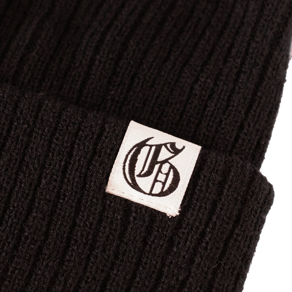 Black knit beanie with a logo tag on a white background