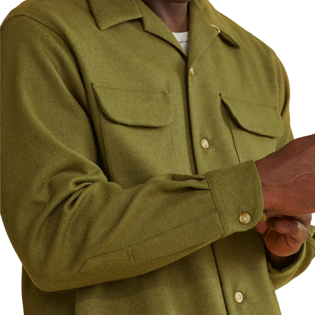 Close-up of a person wearing a long-sleeved olive green Pendleton wool shirt with two front pockets.