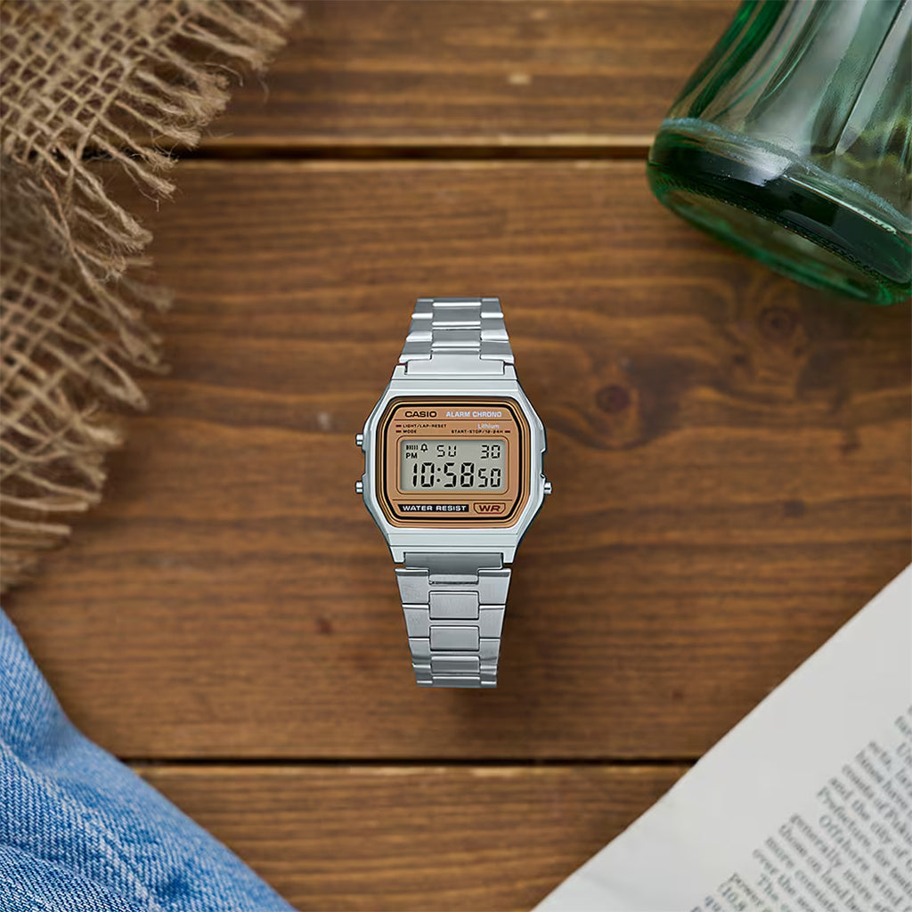 Silver Casio digital watch on a wooden surface with a book and green bottle