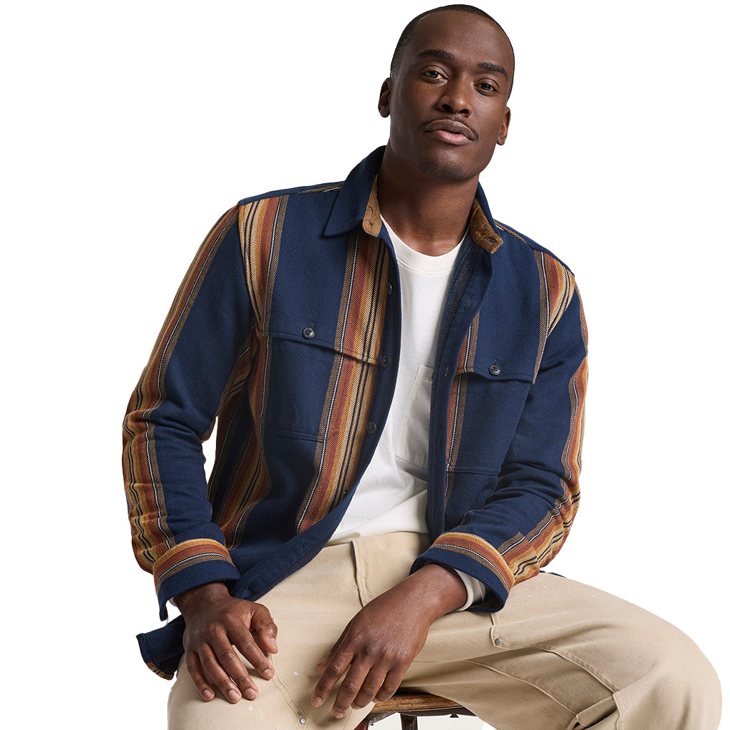 Man wearing a colorful striped shirt over a white t-shirt with beige pants on a white background