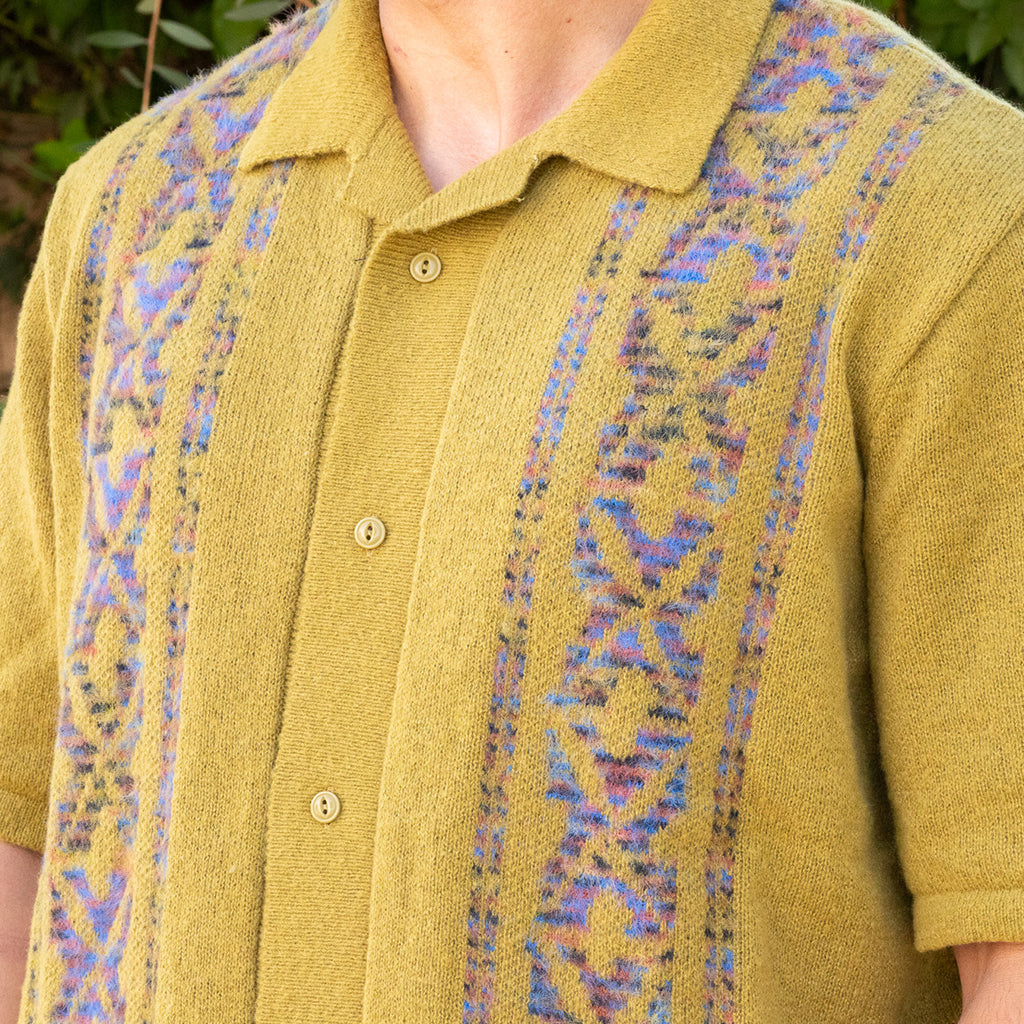 Close-up of a mustard yellow cardigan with patterned trim
