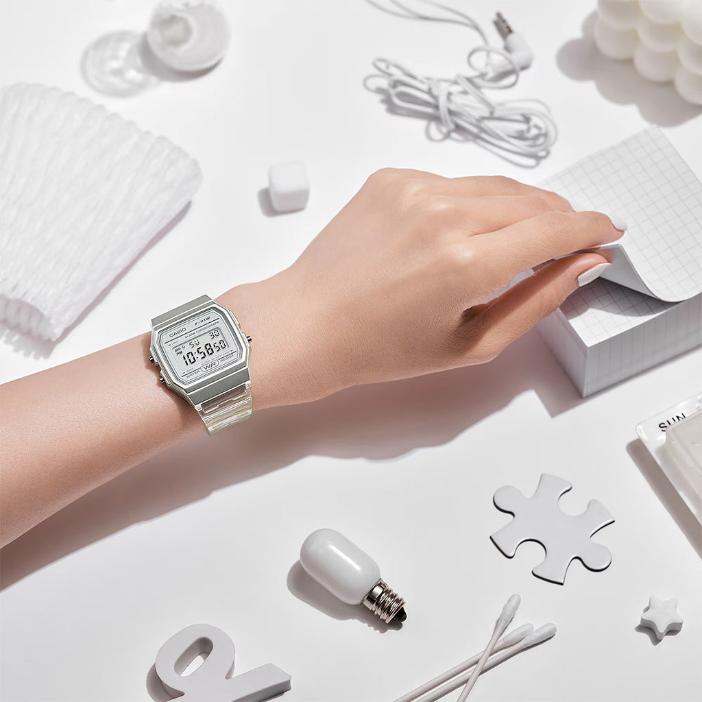 Hand wearing a silver watch on a white surface with minimal objects