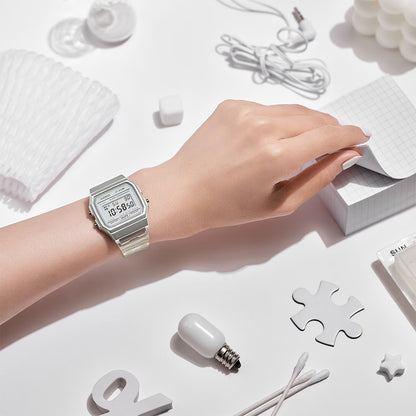 Hand wearing a silver watch on a white surface with minimal objects