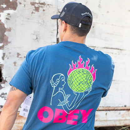 Person wearing a blue t-shirt with a colorful design and 'OBEY' branding, standing against a textured wall.