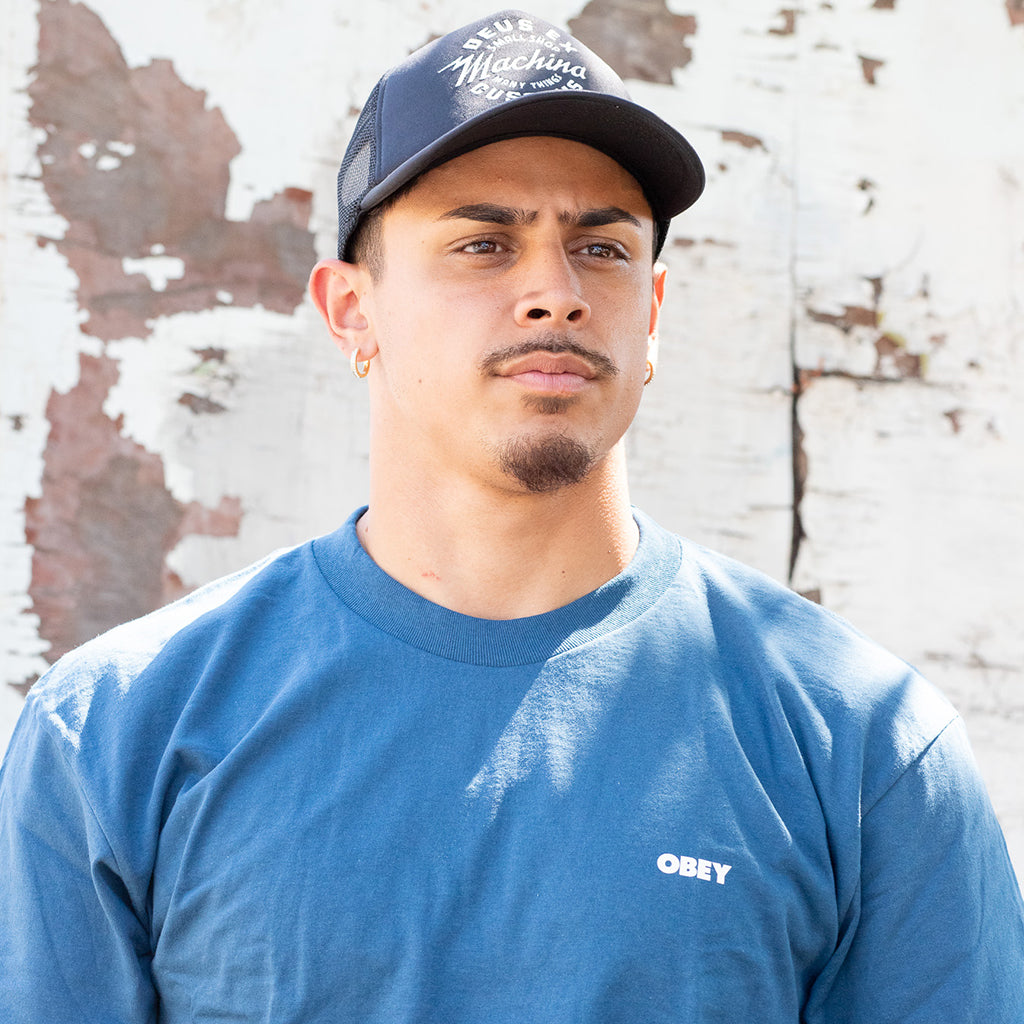 Man wearing a blue cap and OBEY shirt in front of a textured wall