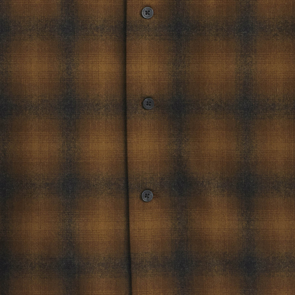 Close-up of a brown and black plaid shirt fabric with buttons.