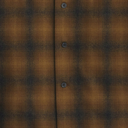 Close-up of a brown and black plaid shirt fabric with buttons.