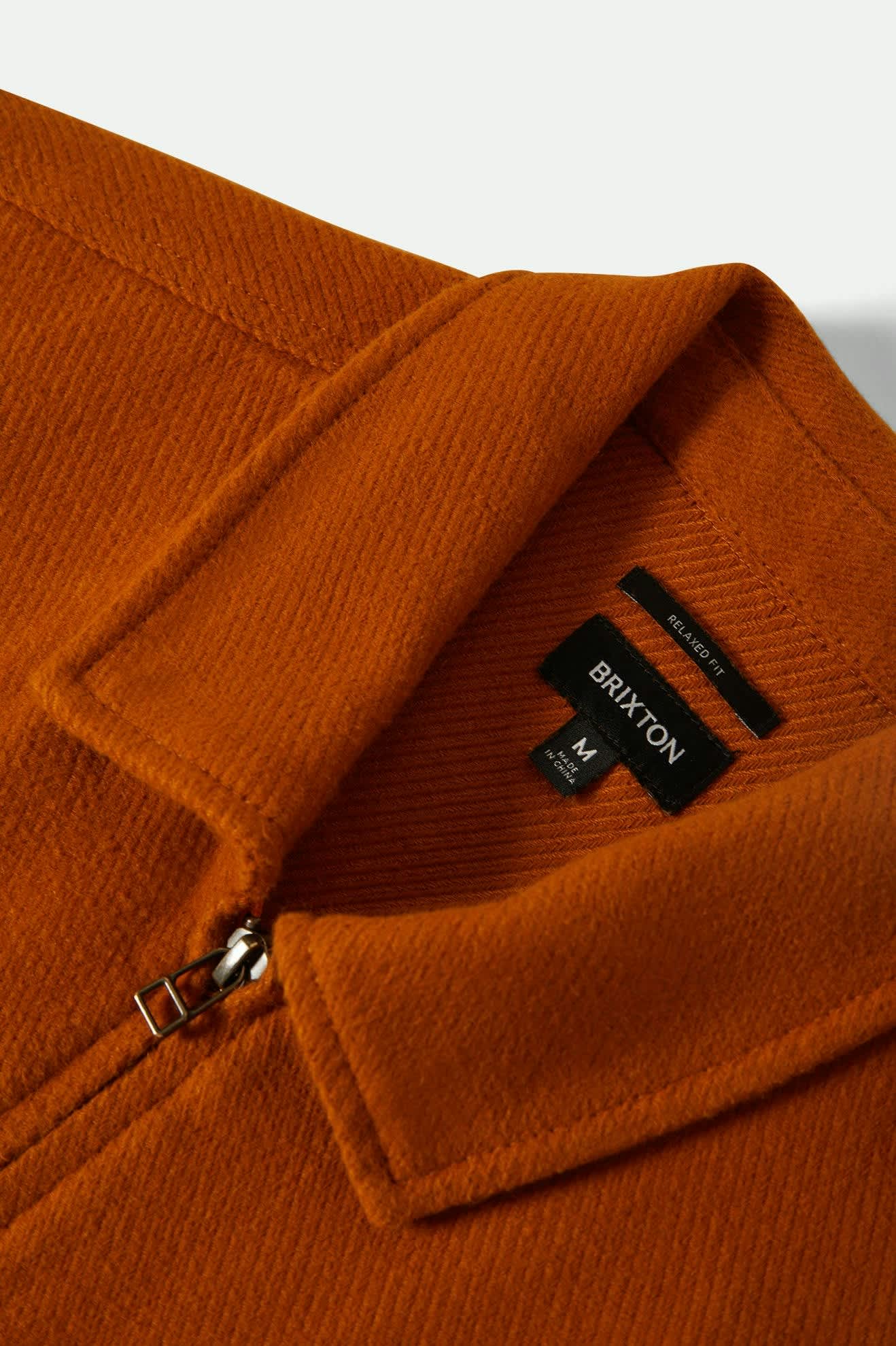 Close-up of an orange jacket with a Brixton label on a white background