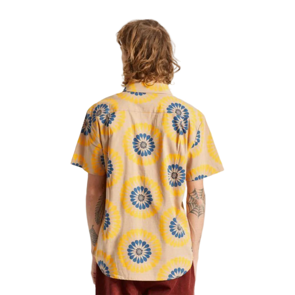 A man viewed from behind wearing a beige short-sleeve button-up shirt with a bold yellow and blue circular floral pattern, paired with burgundy pants, against a plain white background.