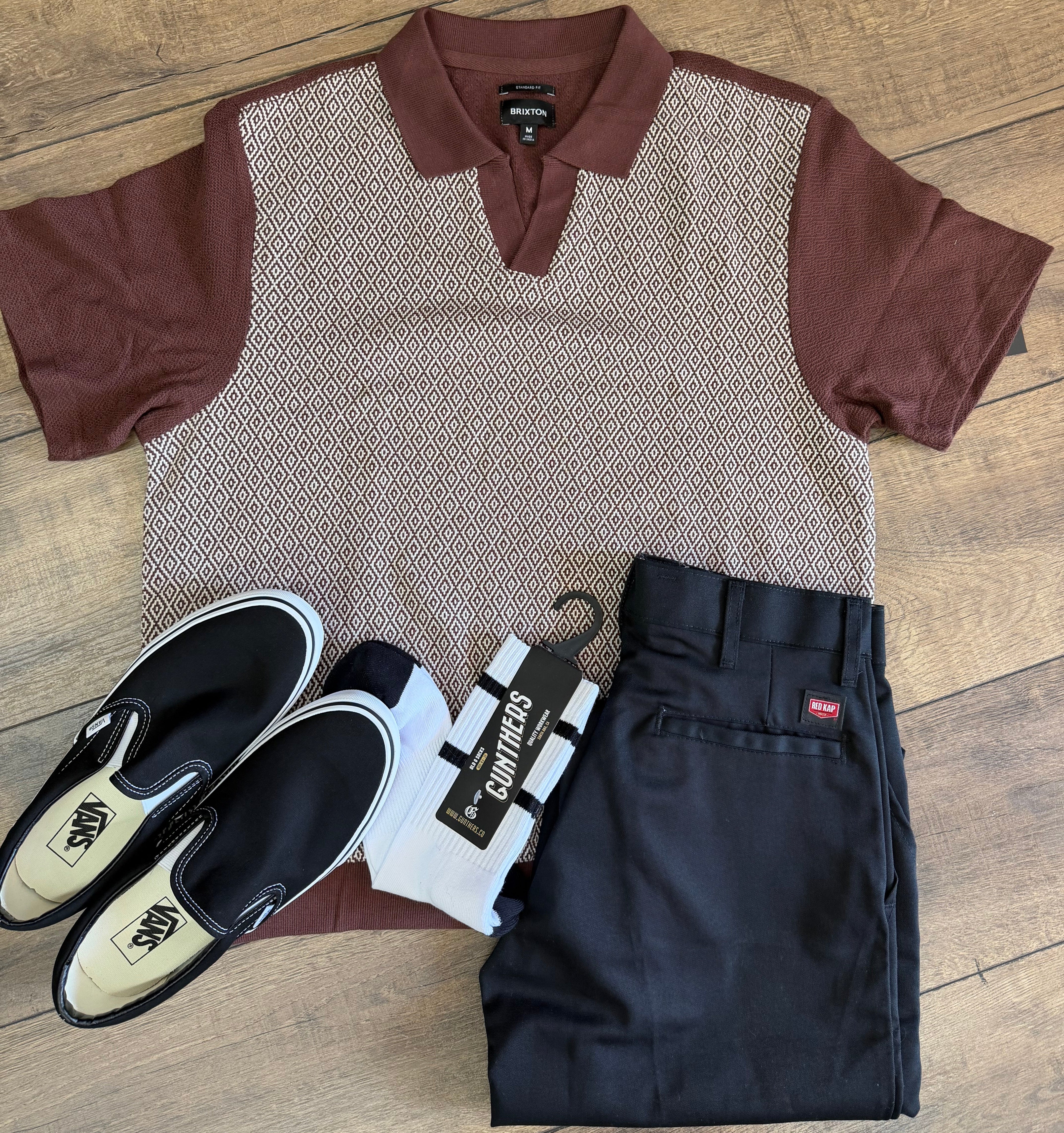 Brown shirt, black pants, white socks, and black shoes on a wooden floor.