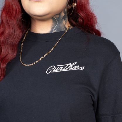 Person wearing a black shirt with 'Gunther' logo and gold chain necklace on gray background
