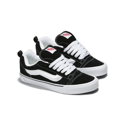 A pair of Vans Knu Skool sneakers with black suede uppers, a puffed up white tongue, white laces, and a black and white checkered pattern on the side stripe.