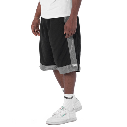 Person wearing black and gray shorts with white sneakers on a white background
