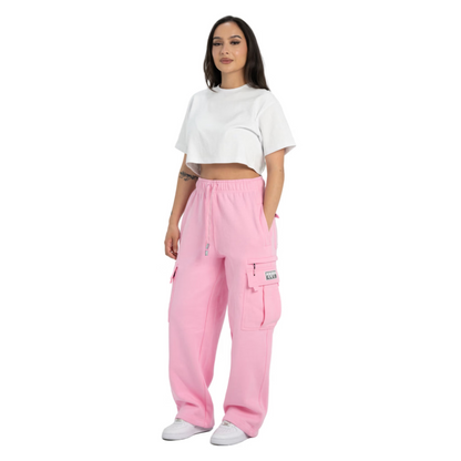 A woman modeling a pair of pink cargo sweatpants with a white cropped t-shirt and white sneakers, standing against a solid white background.