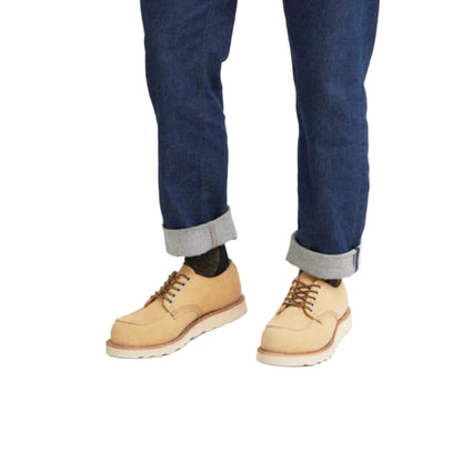 Beige leather shoes worn with rolled-up blue jeans on a white background