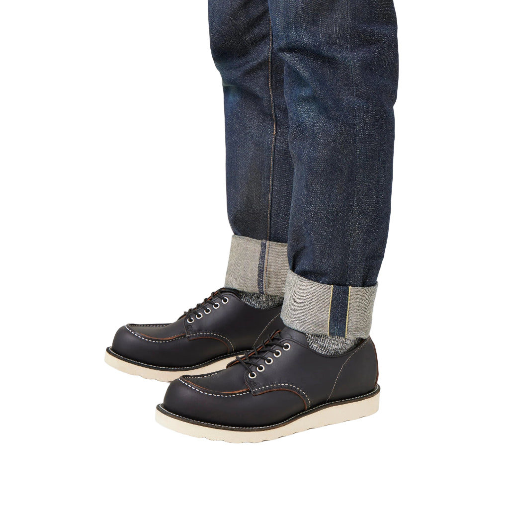 Black leather shoes with white soles worn with blue jeans and gray socks on a white background