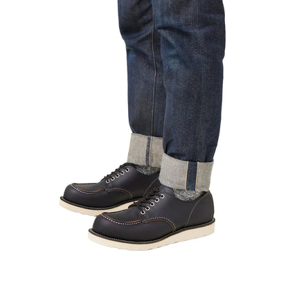 Black leather shoes with white soles worn with blue jeans and gray socks on a white background
