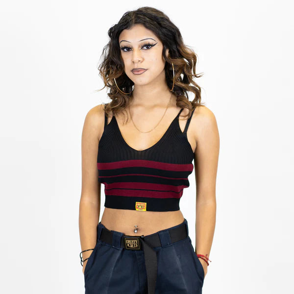 A woman wearing a striped spaghetti strap top in black and burgundy colors, paired with dark pants and accessories.